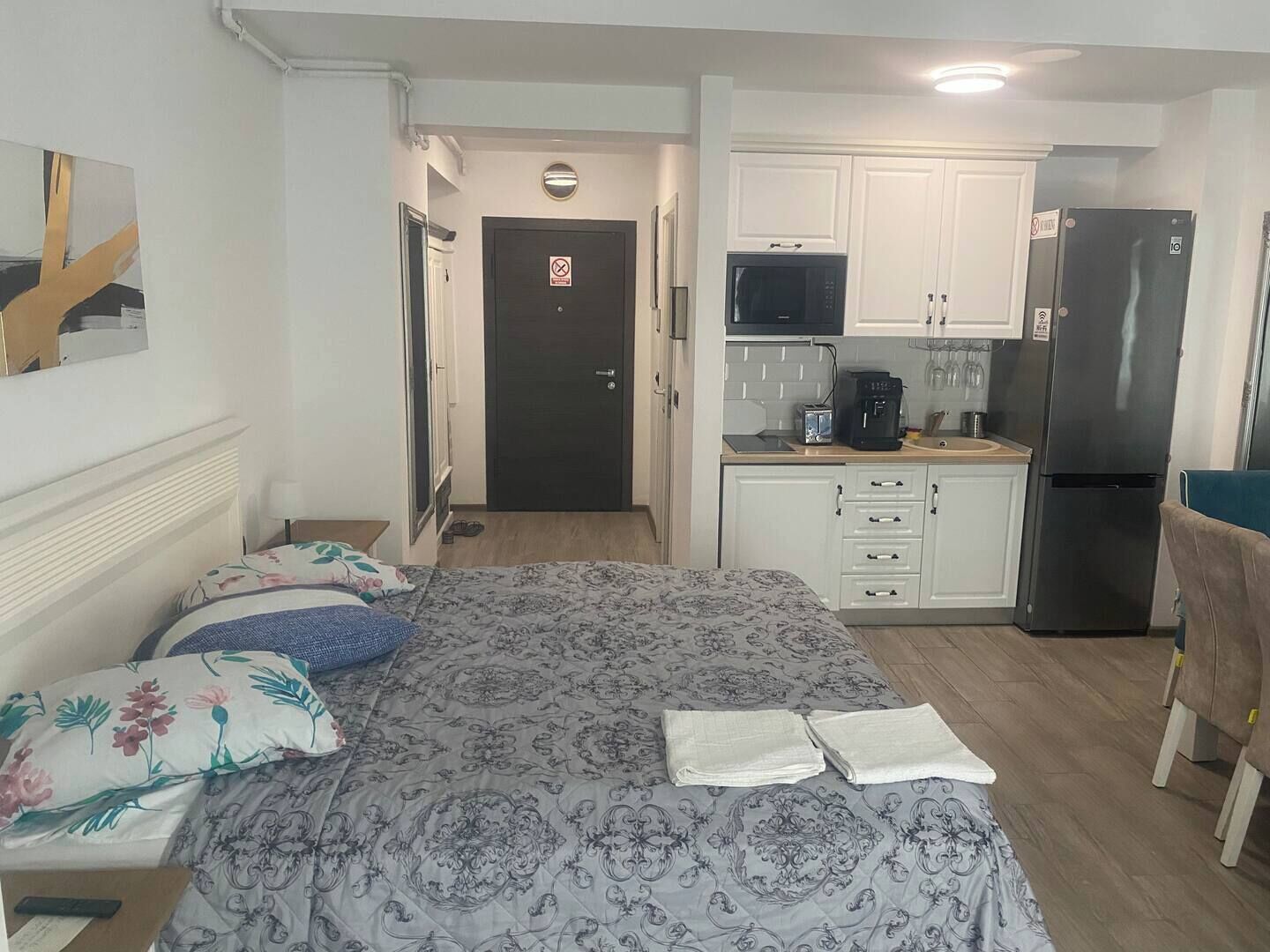A compact room with a bed, a small kitchenette, and a door leading to another room.