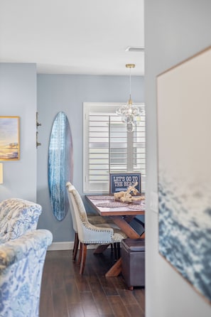 A dining area with a wooden table, chairs, a chandelier, a surfboard, and a sign.