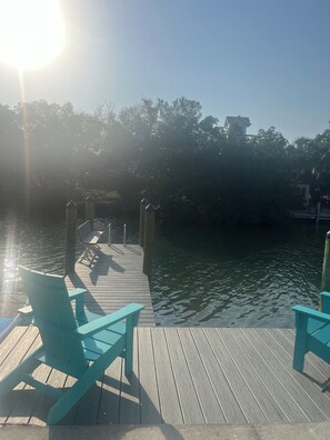 A wooden dock extending into calm water, with two turquoise chairs and a bench.