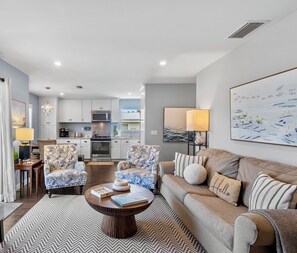 A modern living room with a sofa, armchairs, a coffee table, and a kitchen in the background.