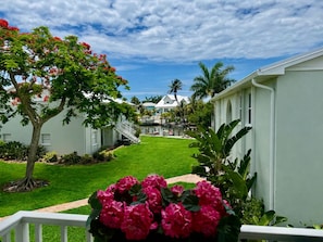 A residential area with a well-maintained lawn, a tree with red flowers, and a white building with a balcony. - 2BR Waterfront with Dock. Best area in Anna Maria. Beach, Sunsets on Pine Ave. (Anna Maria)