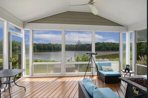 Un espacio al aire libre techado con vista a un lago, un telescopio, una mesa y un sofá.