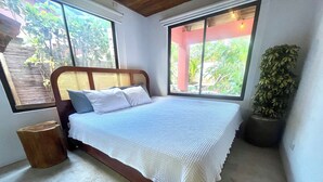 Une chambre à coucher avec un cadre de lit en bois, du linge de lit blanc et une grande fenêtre donnant sur un paysage verdoyant.
