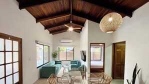 Une pièce spacieuse avec un plafond haut, une table ronde en verre entourée de chaises en osier, un canapé et un téléviseur.