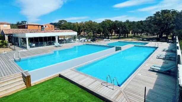 Una piscina rectangular grande con cubierta de madera y un área verde frente a ella.