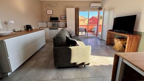 Un espacio habitable compacto con kitchenette, un sofá, un televisor y una puerta corrediza de vidrio que da a un área exterior.