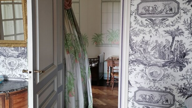 A hallway with patterned wallpaper, a wooden door, and a dining area with a table and chairs. - Manoir de Villers (Saint-Pierre-de-Manneville)