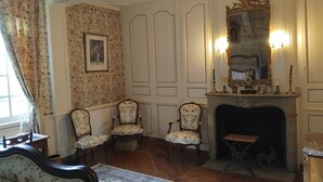 A room with a fireplace, floral-patterned chairs, a table, and a framed picture on the wall. - Manoir de Villers (Saint-Pierre-de-Manneville)