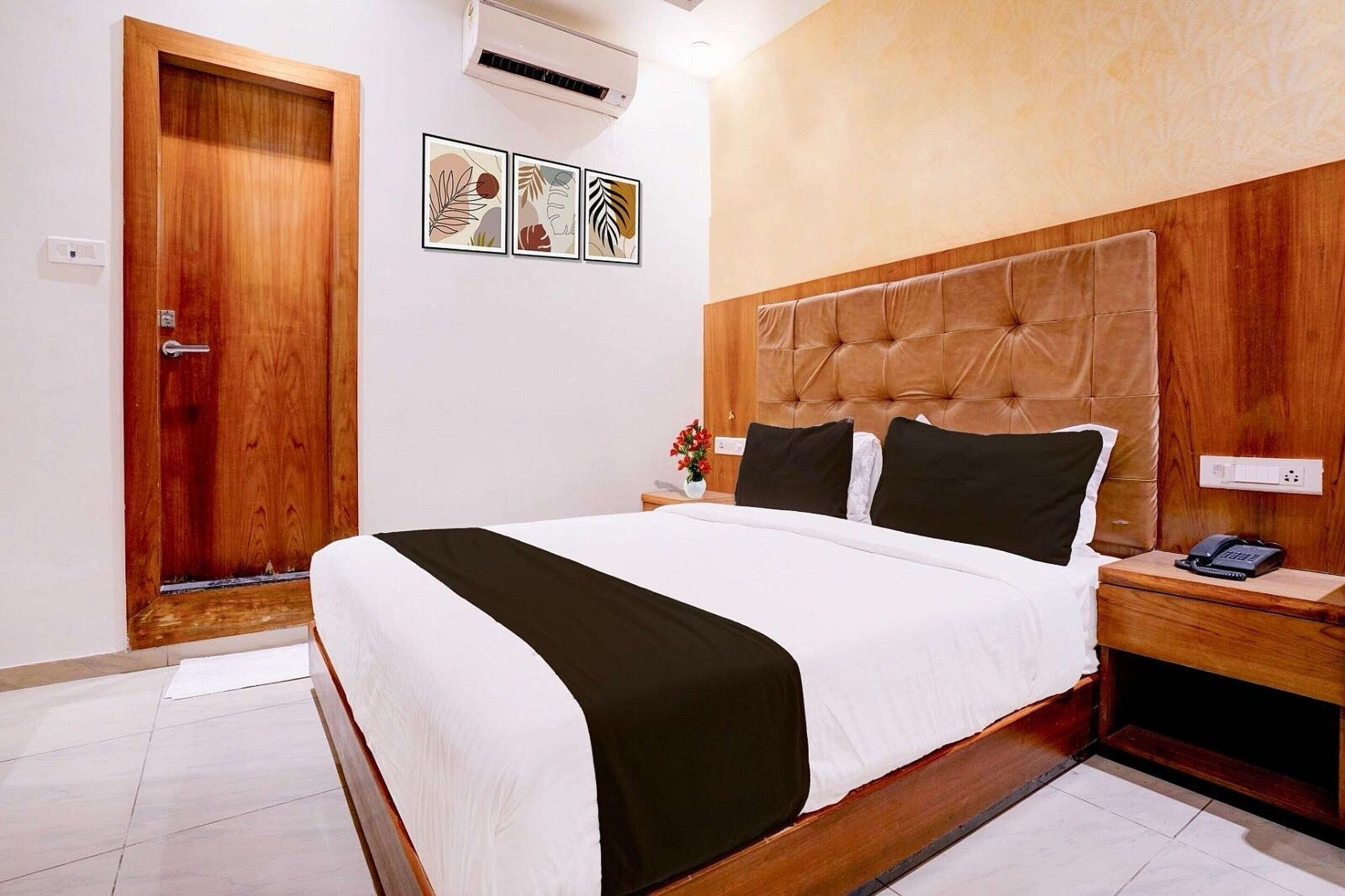 A hotel room with a wooden bed, a nightstand, a telephone, and a wall-mounted air conditioner.
