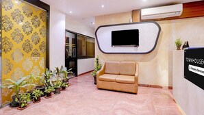 Een ontvangsthal met een bank, potplanten, een aan een muur bevestigde televisie en een bordje met de tekst 'Company Serviced'.