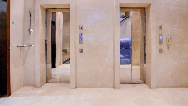 Een moderne lift met een metalen afwerking en een glazen deur, die het interieur weerspiegelt.