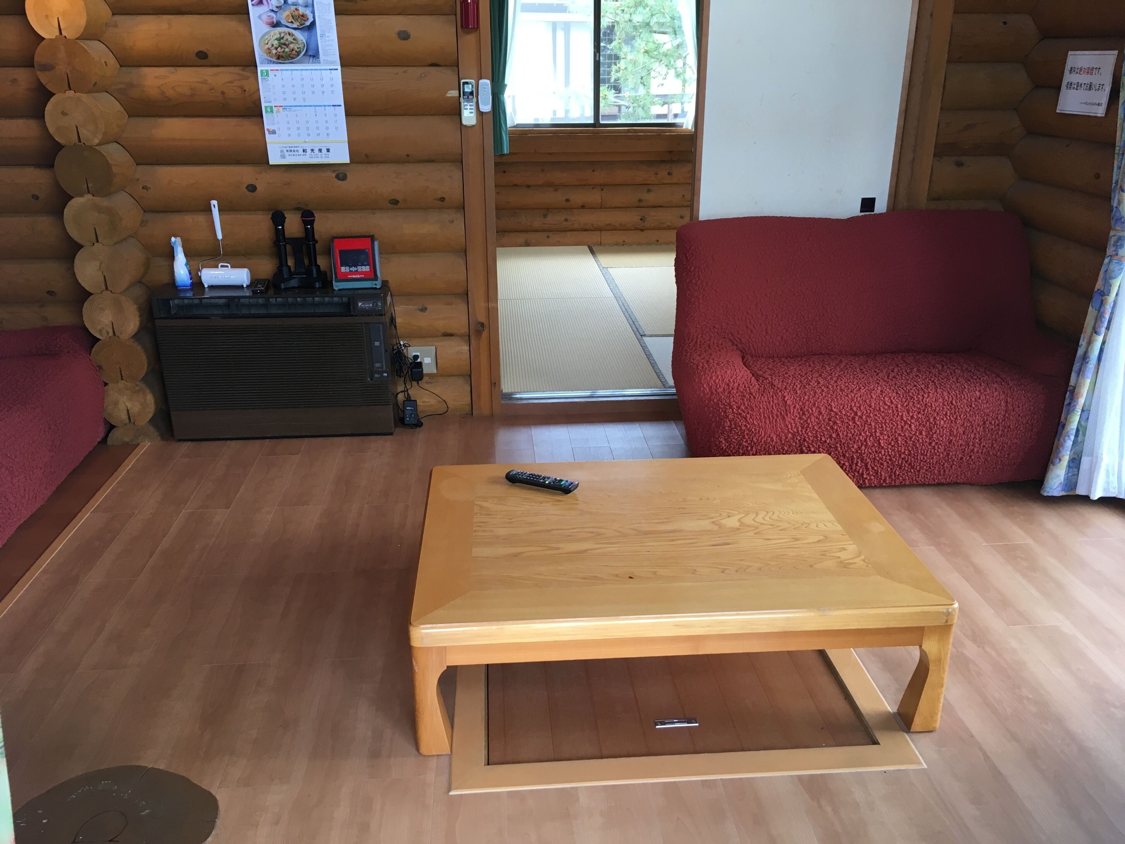 A log cabin interior with a wooden table, a red sofa, a wooden cabinet with electronic devices, and a calendar on the wall.