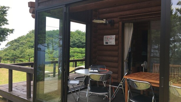 A wooden cabin with a glass door leading to an outdoor deck. Inside, there is a round table with chairs and a small table with a chair. - Heartland Hills in Noto 31 Umi no Canadian House (Nanao)