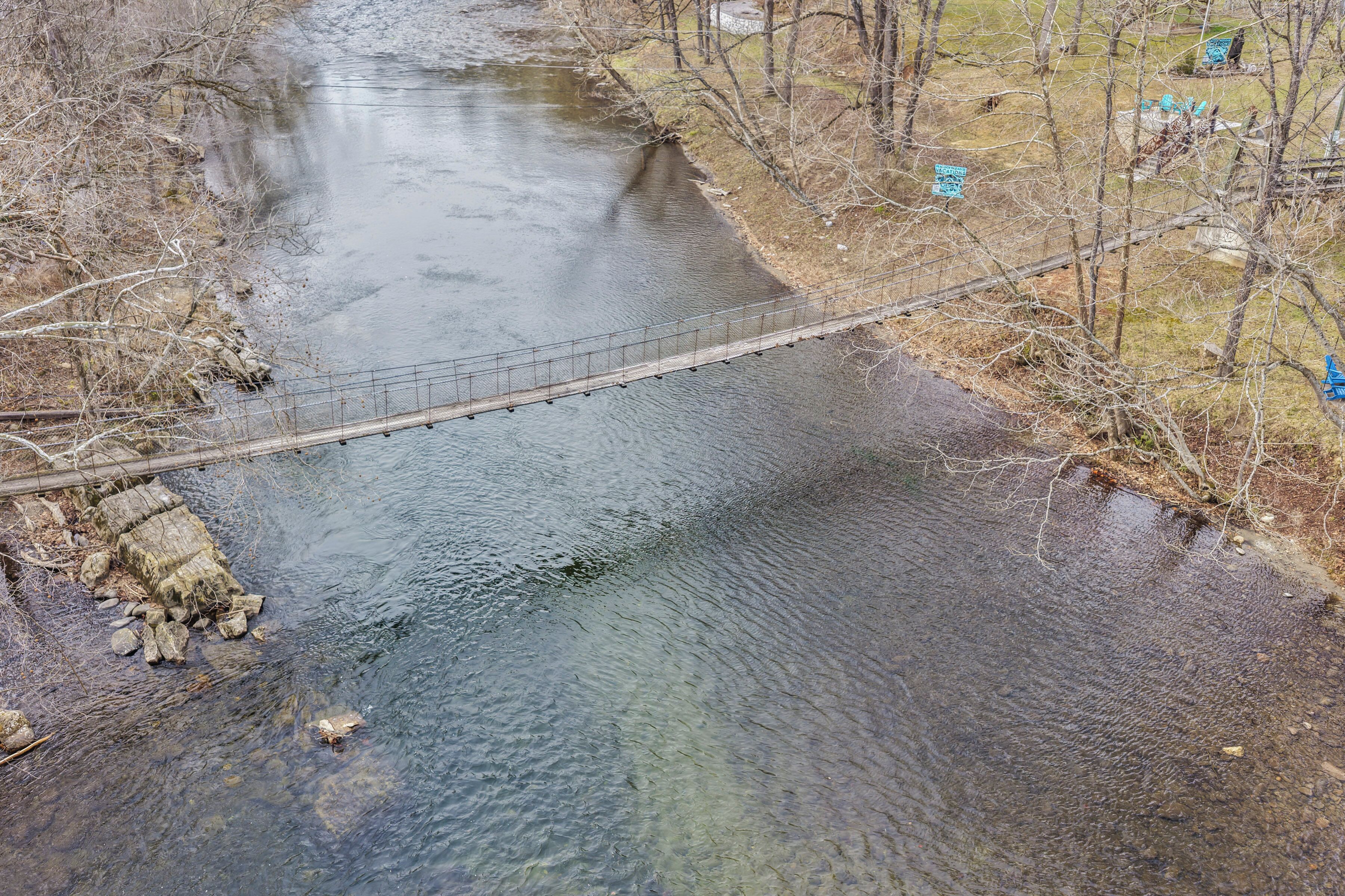 A river with a bridge, surrounded by trees and some buildings in the background.