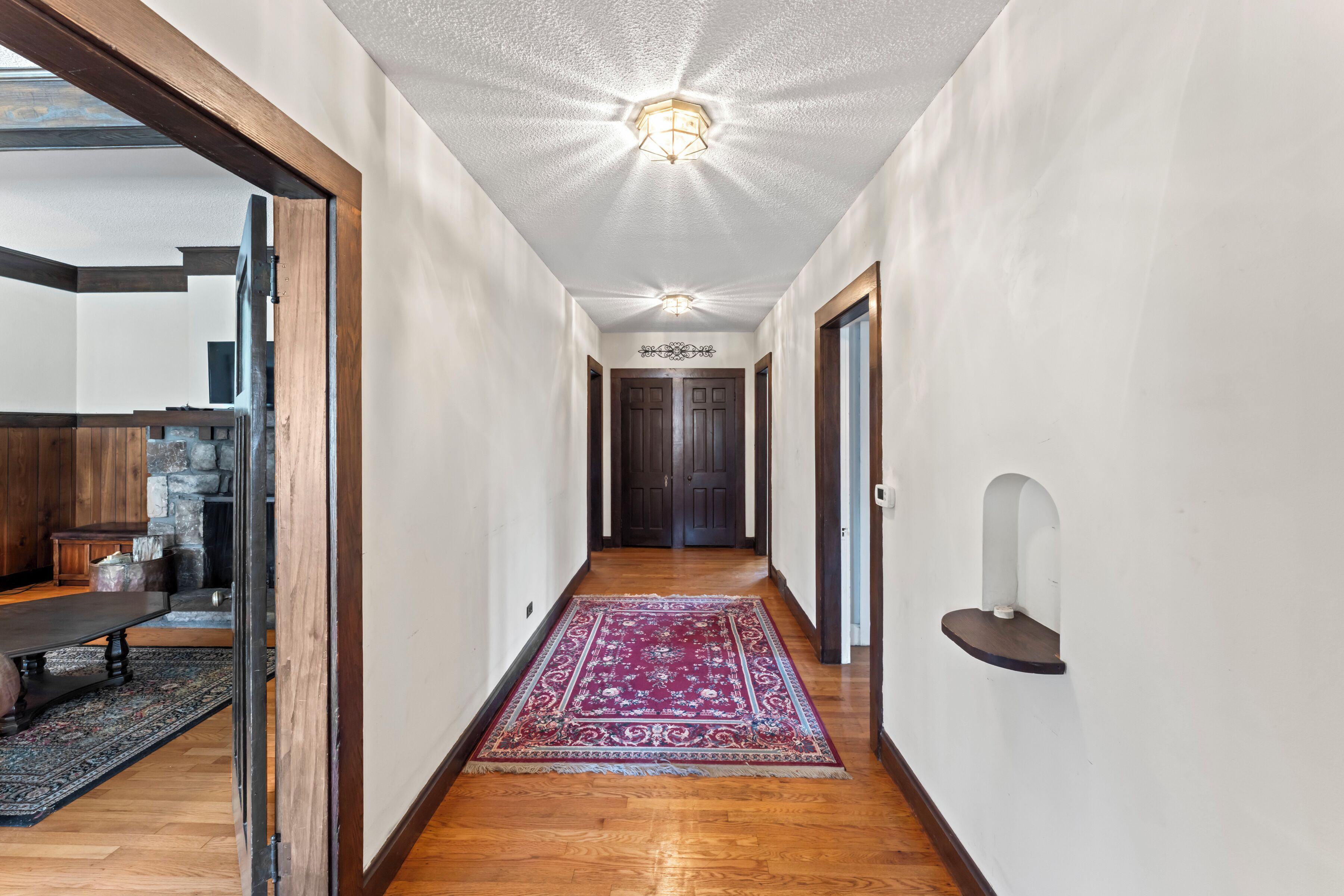 A hallway with wooden flooring, a red patterned rug, and a ceiling light fixture.