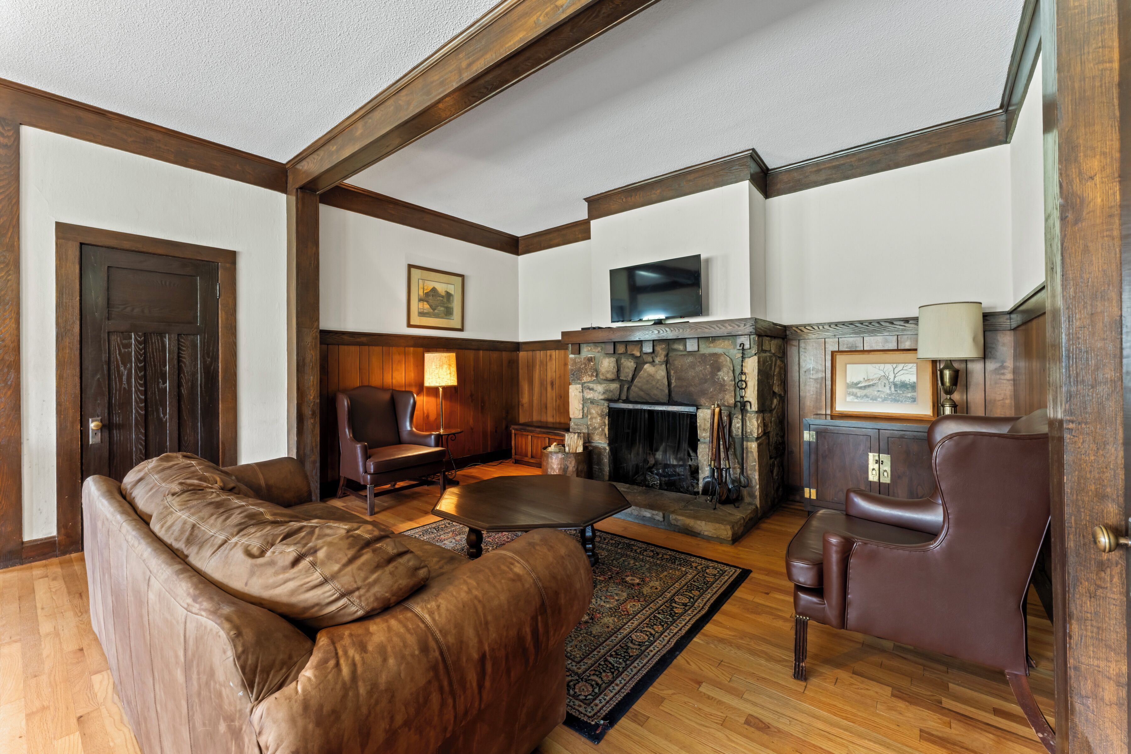 A living room with a stone fireplace, leather furniture, and wooden beams on the ceiling.