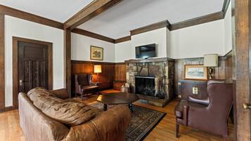 A living room with a stone fireplace, leather furniture, and wooden beams on the ceiling.