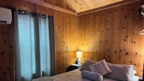 A wooden-paneled room with a bed, curtains, a nightstand, and a lamp. - Tiny Home II, Pet Friendly, Free Cancellations (Boone)