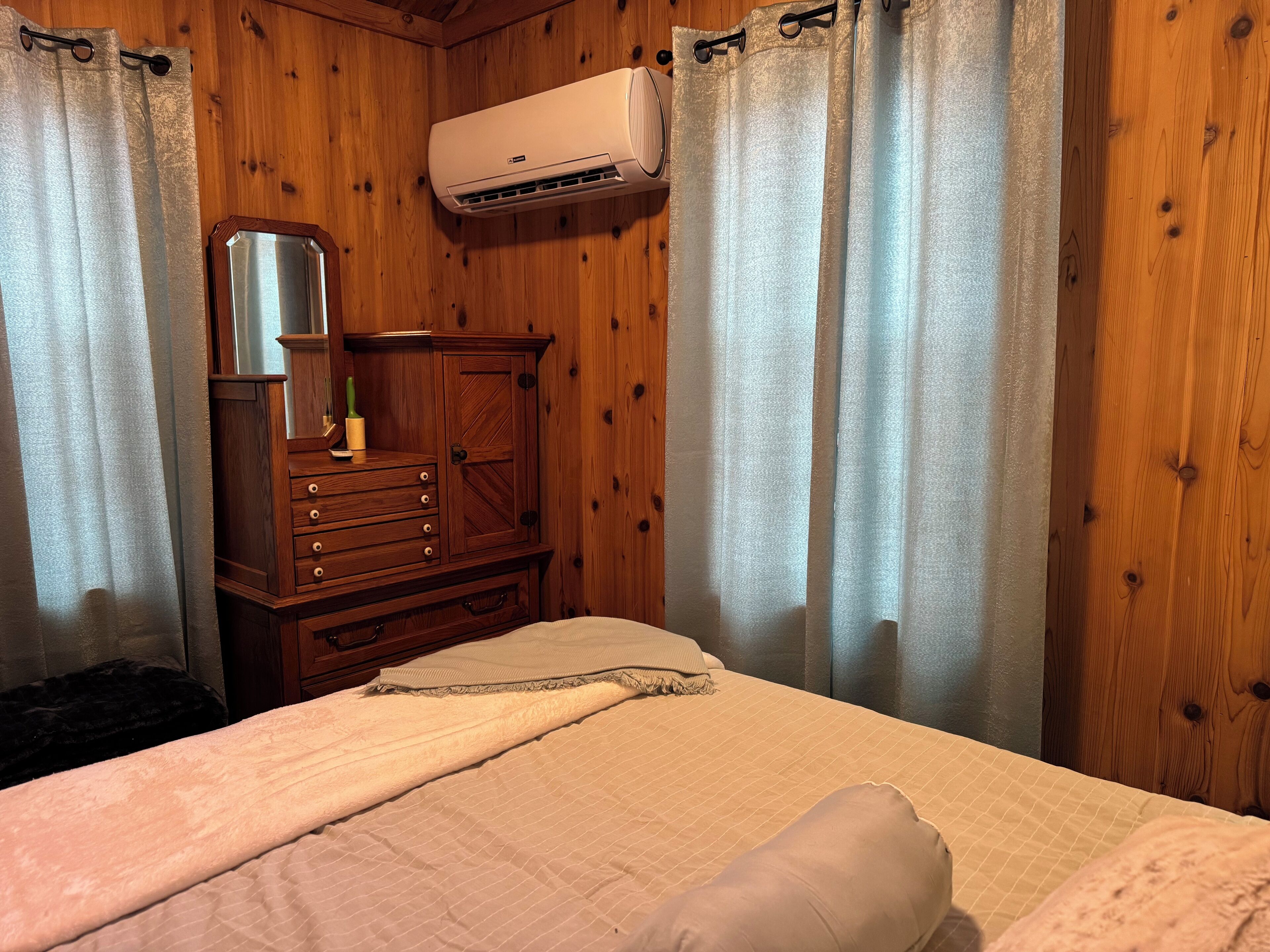 A bedroom with a bed, a wooden dresser, a mirror, and an air conditioning unit.