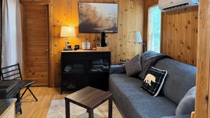 A cozy cabin interior with a wooden ceiling, a sofa, a small table, a lamp, a coffee station, and a painting. - Tiny Home II, Pet Friendly, Free Cancellations (Boone)