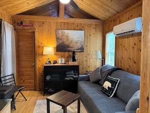 Interior acolhedor de uma cabana com teto de madeira, um sofá, uma mesinha, um abajur, um espaço para café e um quadro.