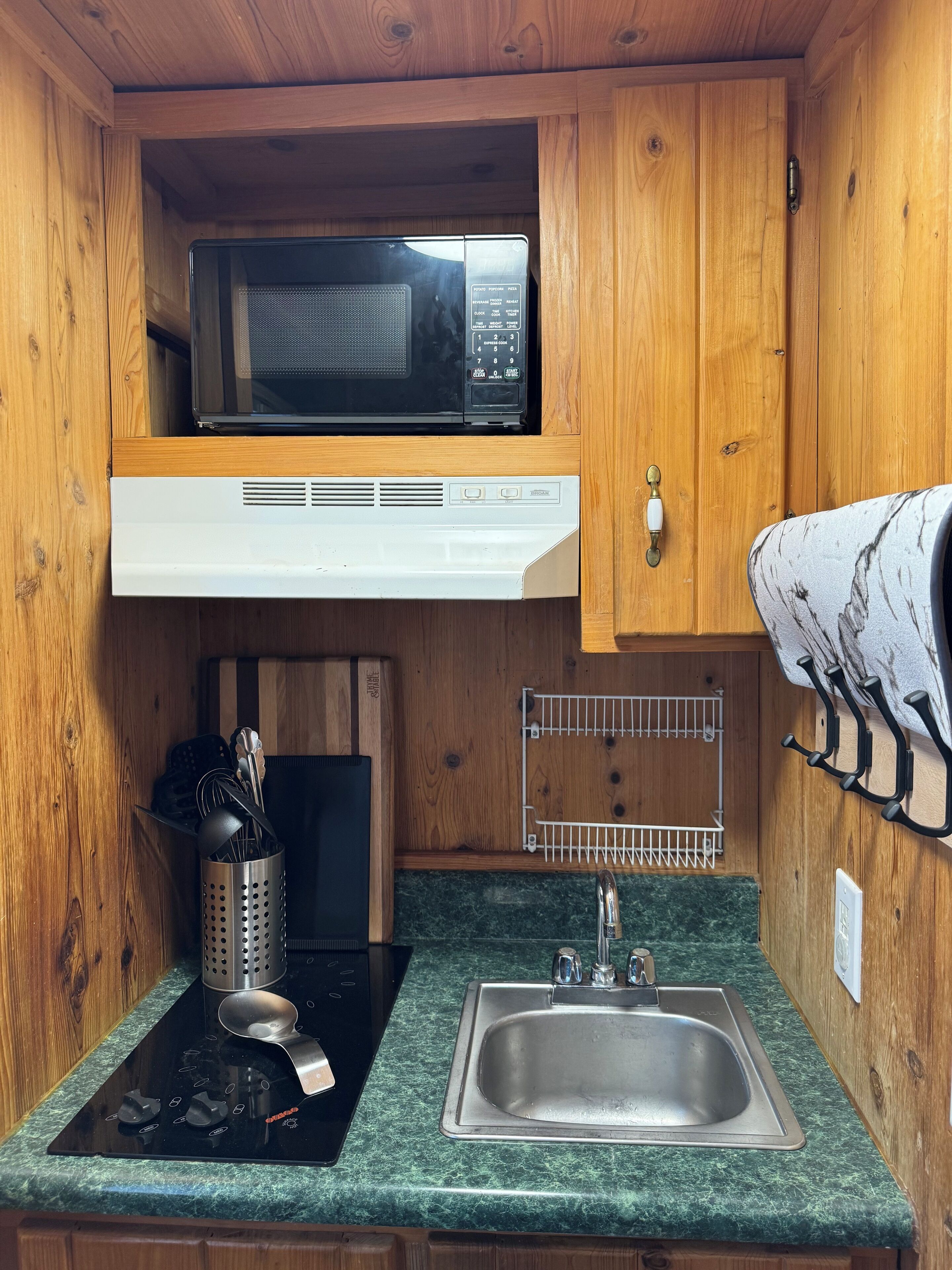 A compact kitchen with a microwave, stove, sink, and wooden cabinets.