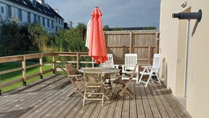 Um deck de madeira com mobiliário de exterior, incluindo uma mesa e cadeiras, e um guarda-sol vermelho.