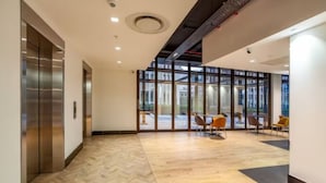 A spacious lobby with a herringbone patterned floor, a glass wall offering a view of the street, and a seating area with chairs. - Modern Foreshore Apartment | City Views, WiFi & Parking (Cape Town)