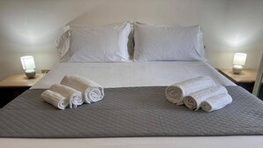 A neatly made bed with white linens and two rolled towels on the bed. There are two bedside tables with lamps on either side of the bed. - Apartment in a Villa With a Relaxing Pool (Ispica)