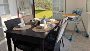 A dining area with a table set for two, a high chair, and a view of greenery outside. - Apartment in a Villa With a Relaxing Pool (Ispica)