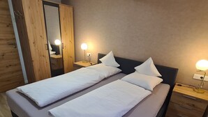 Ein Doppelbett mit weißer Bettwäsche, zwei Nachttische mit Lampen, ein Holzschrank und ein Spiegel.