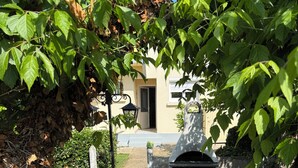 A patio with a round table and chairs, a stone barbecue, and a building in the background. - Cosy house with garden - near Mimizan beach (Mimizan)