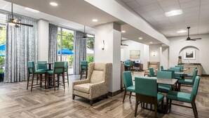 Un hall d’hôtel spacieux au design moderne, comprenant différents espaces de détente et une cuisine en arrière-plan.