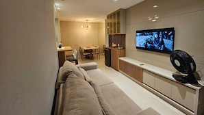 A modern living room with a sofa, TV, and dining area. - Apto 2 Quartos com 1 Suíte a Poucos Passos da Praia (Vila Velha)