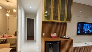 A modern kitchen with a built-in refrigerator, wooden paneling, and a glass-fronted cabinet above the counter. - Apto 2 Quartos com 1 Suíte a Poucos Passos da Praia (Vila Velha)