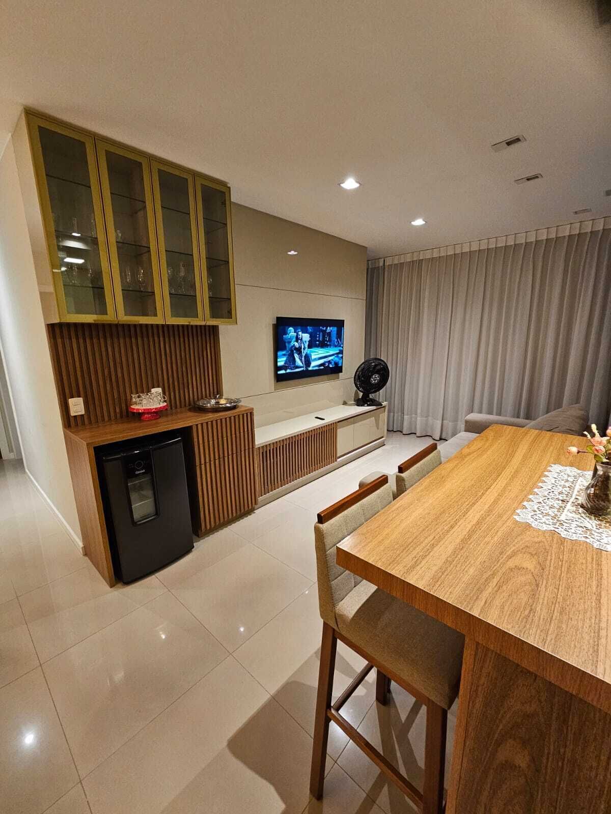 Uma cozinha moderna com máquina de lavar louça embutida, área de refeições com mesa e cadeiras de madeira, e uma TV fixada na parede.
