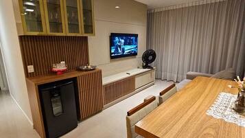 Uma cozinha moderna com máquina de lavar louça embutida, área de refeições com mesa e cadeiras de madeira, e uma TV fixada na parede.