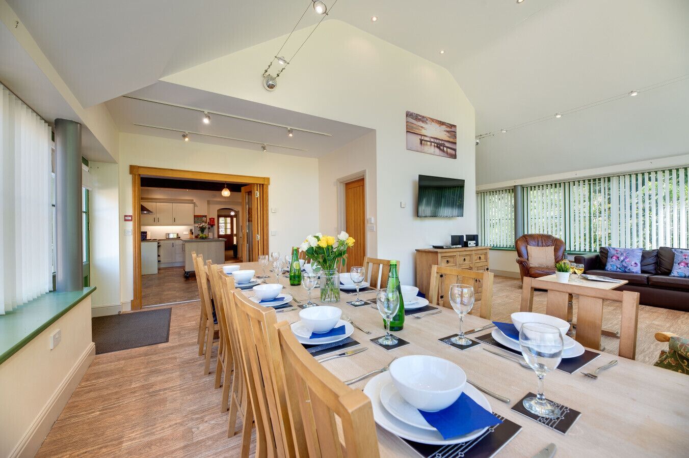 A spacious dining area with a long table set for a meal, a cozy living area with a sofa and a television, and a kitchen in the background.