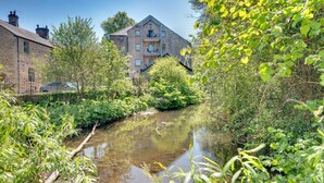 Een smalle waterweg omringd door weelderige begroeiing, met een gebouw met meerdere verdiepingen en balkons.