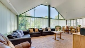 Een ruime woonkamer met een grote zwarte bank, een houten salontafel en een eettafel met stoelen.