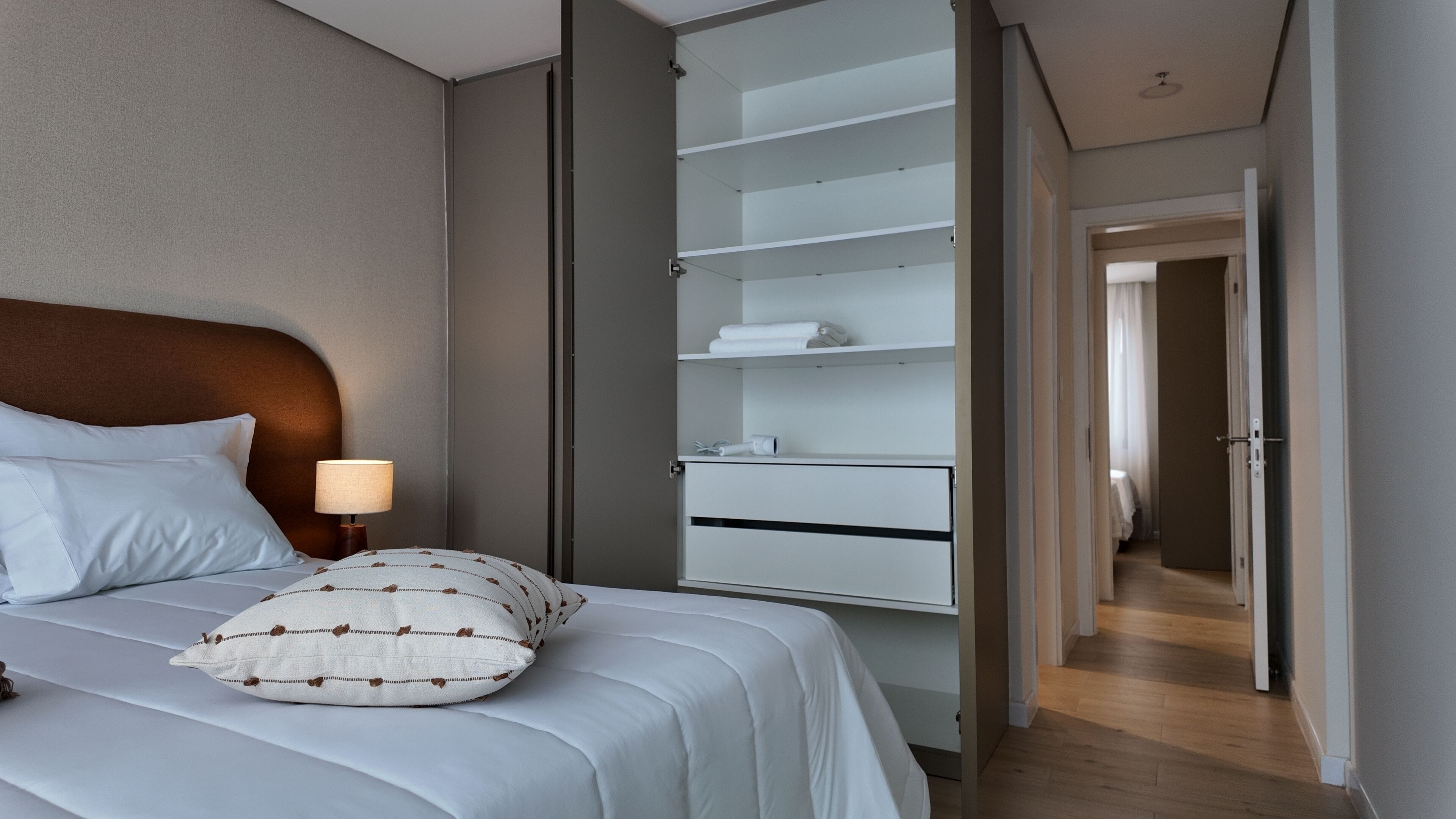 A hotel room with a bed, a nightstand, a lamp, a wardrobe, and a hallway.