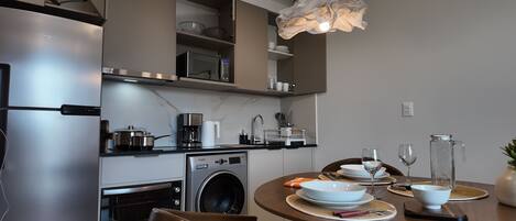 A modern kitchen with a stainless steel refrigerator, a built-in oven, a microwave, a washing machine, and a dining area with a round table set for two.