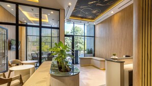 A modern hotel lobby with a reception desk, seating area, large windows, and a ceiling with decorative elements. - Well Residences - By AVA Rentals (Asunción)