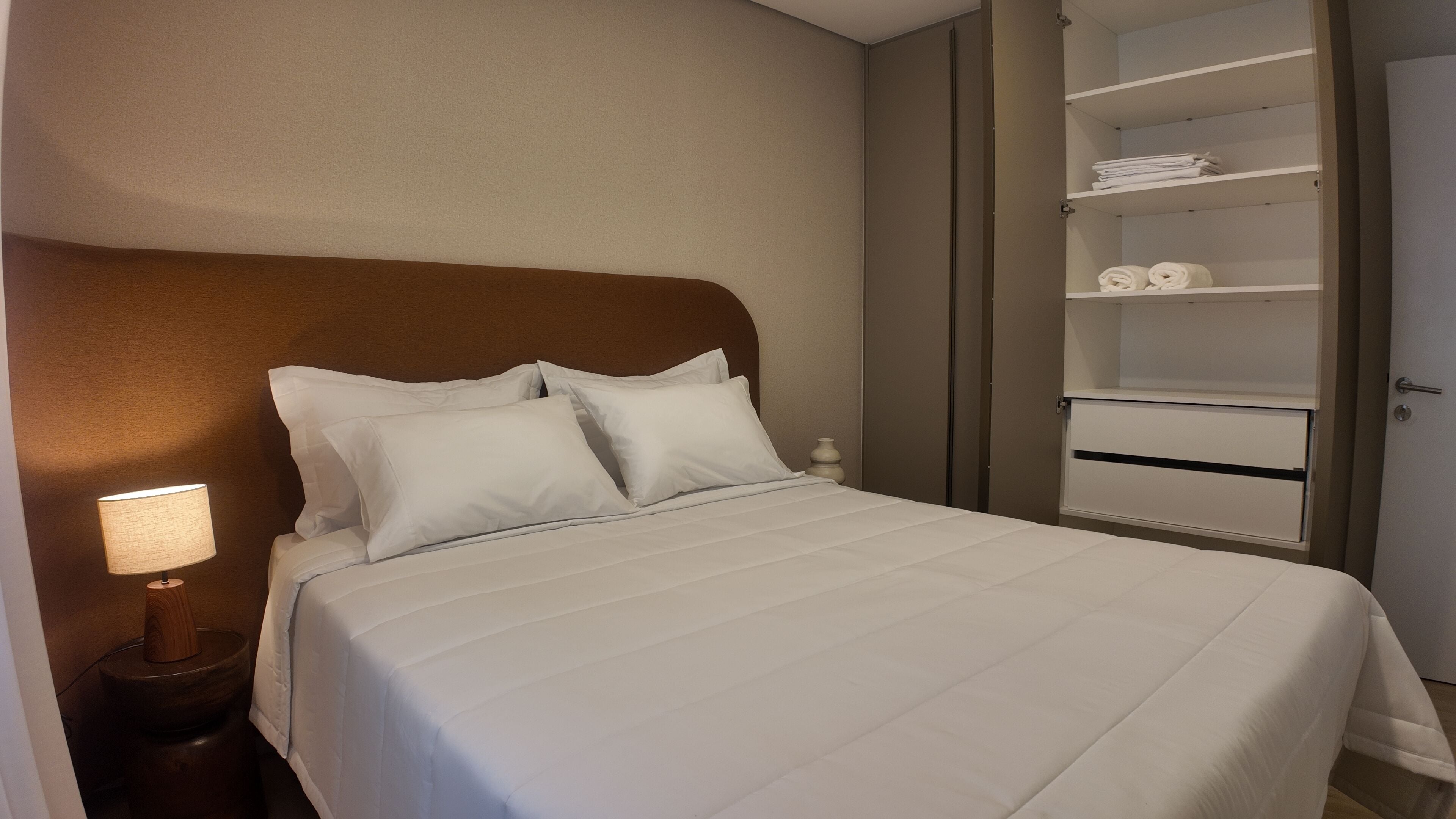A neatly made bed with white linens, a wooden headboard, and a bedside lamp.
