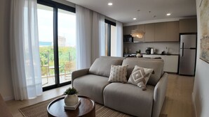 A modern living room with a sofa, a coffee table with a plant, and a view of a cityscape through large windows. - Well Residences - By AVA Rentals (Asunción)