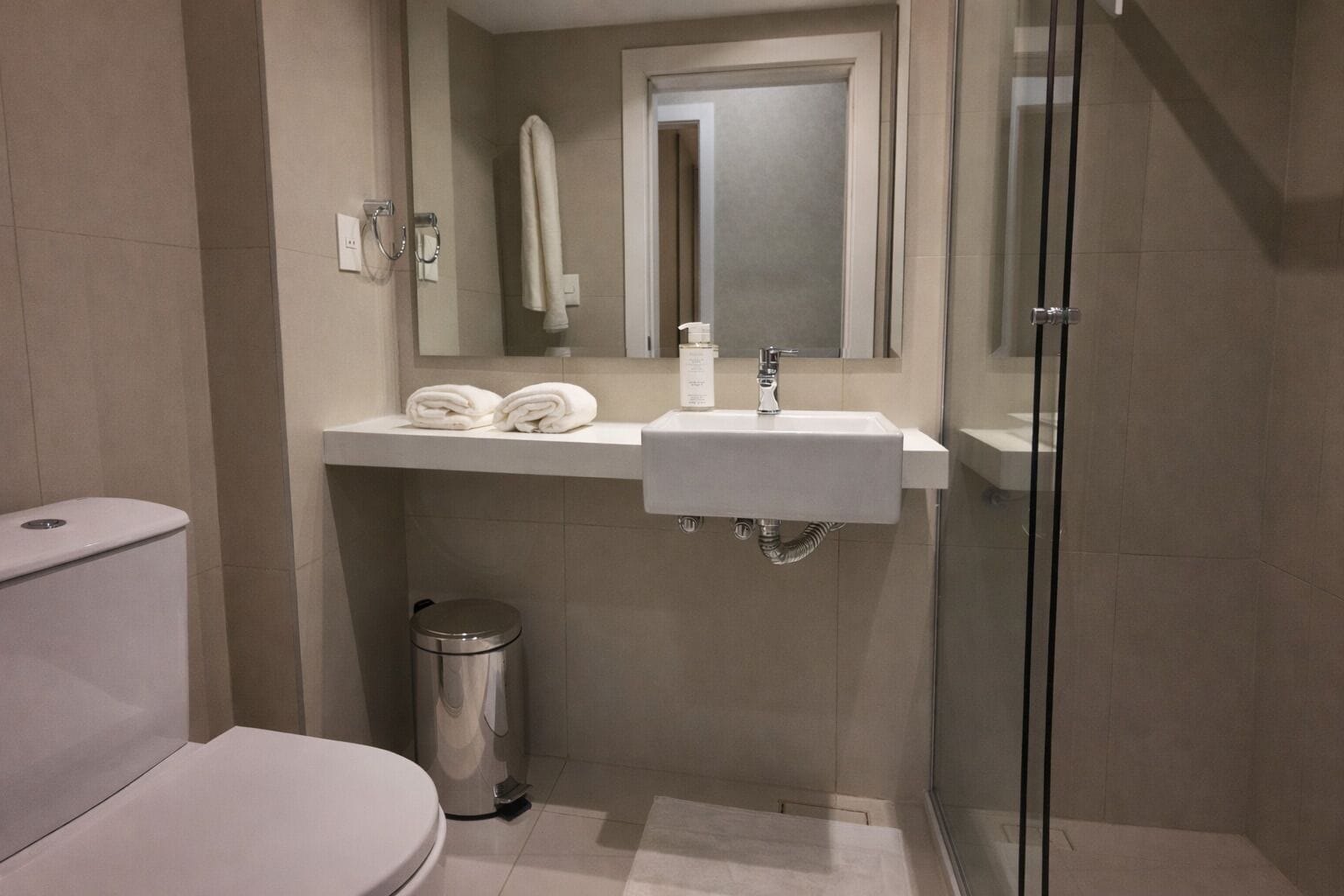Et moderne badeværelse med toilet, vask, spejl og glasvæg ved brusebad.
