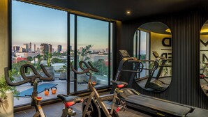 A gym with exercise equipment, a large window with a city view, and a mirror reflecting the equipment. - Well Residences - By AVA Rentals (Asunción)
