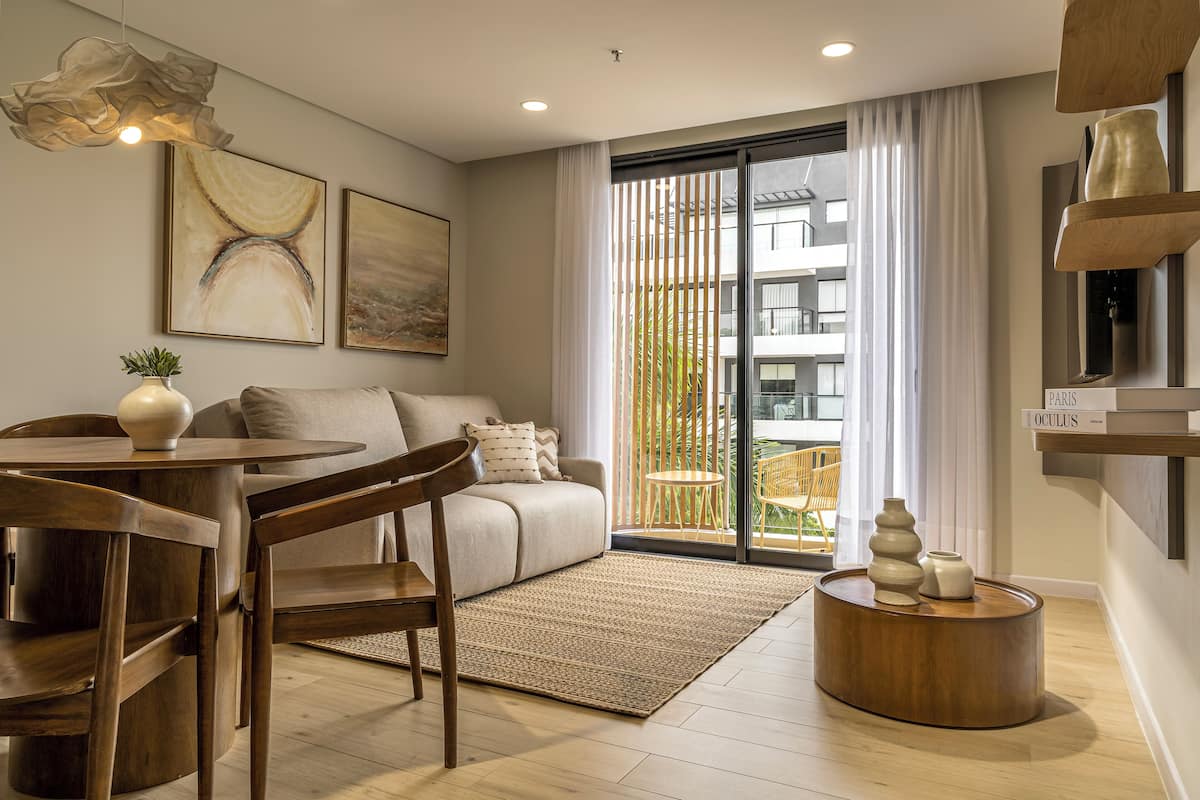 A modern living room with a sofa, dining table, chairs, a coffee table, artwork, and a view of a balcony.