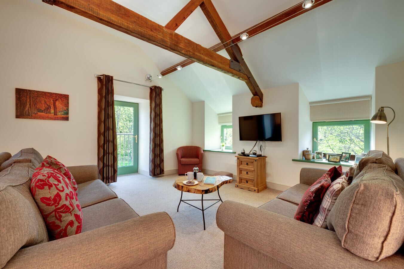 Ein gemütliches Wohnzimmer mit hohen Decken, Holzbalken, einem Fernseher, einem Sofa, einem Sessel und einem kleinen Tisch mit Tablett.