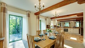 Un coin repas avec une table en bois dressée pour quatre personnes, une cuisine en arrière-plan et un balcon avec une chaise.